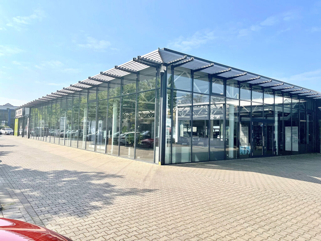 Außenansicht eines modernen Autohauses mit großen Glasfronten und einer überdachten Einfahrt.